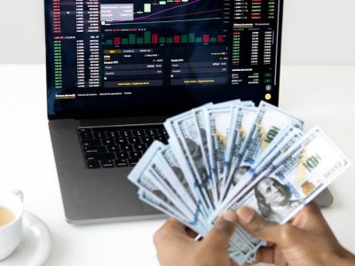 Hands holding cash in front of a laptop displaying stock market data, symbolizing financial growth and investment.